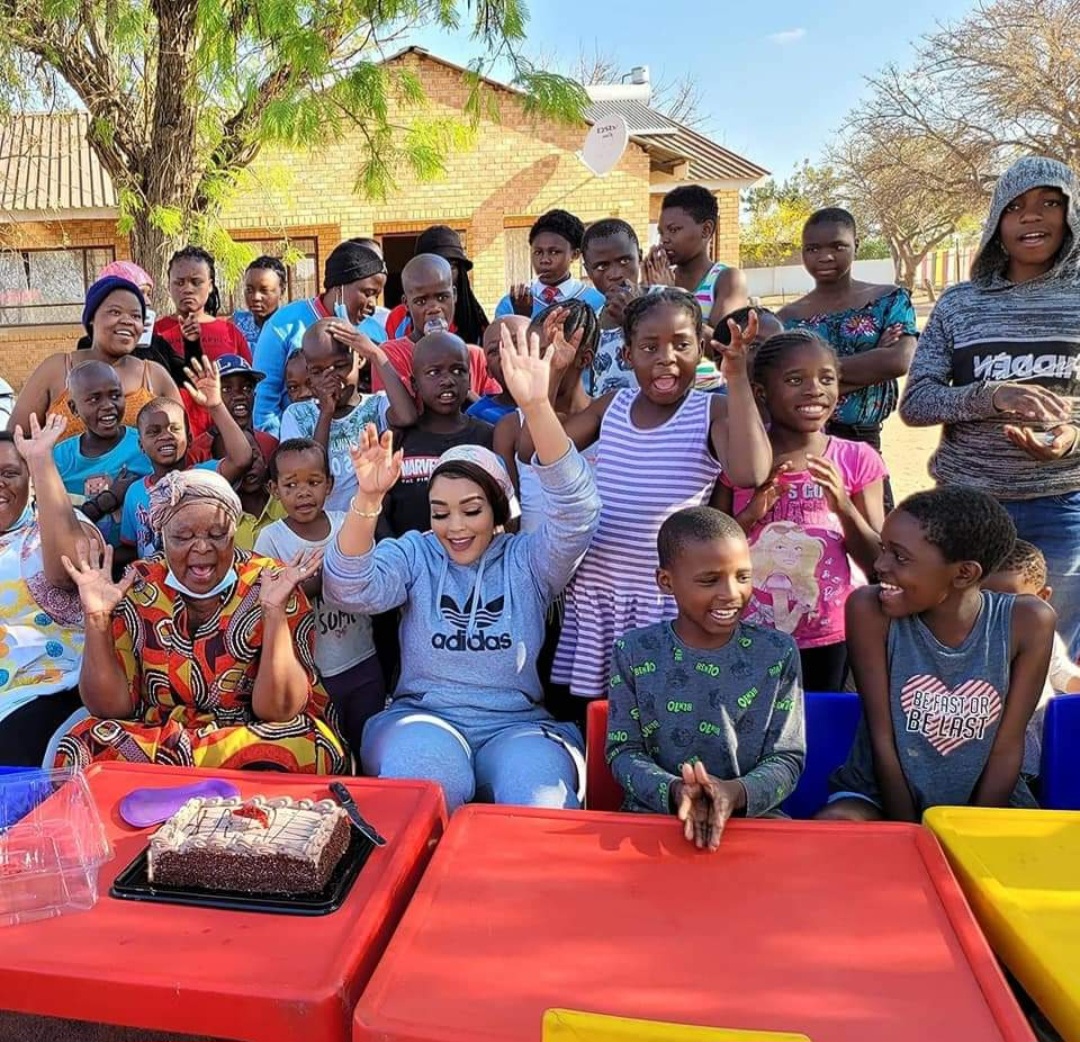 Zari Hassan with a group of children and elders gathered around a birthday cake outside a community home