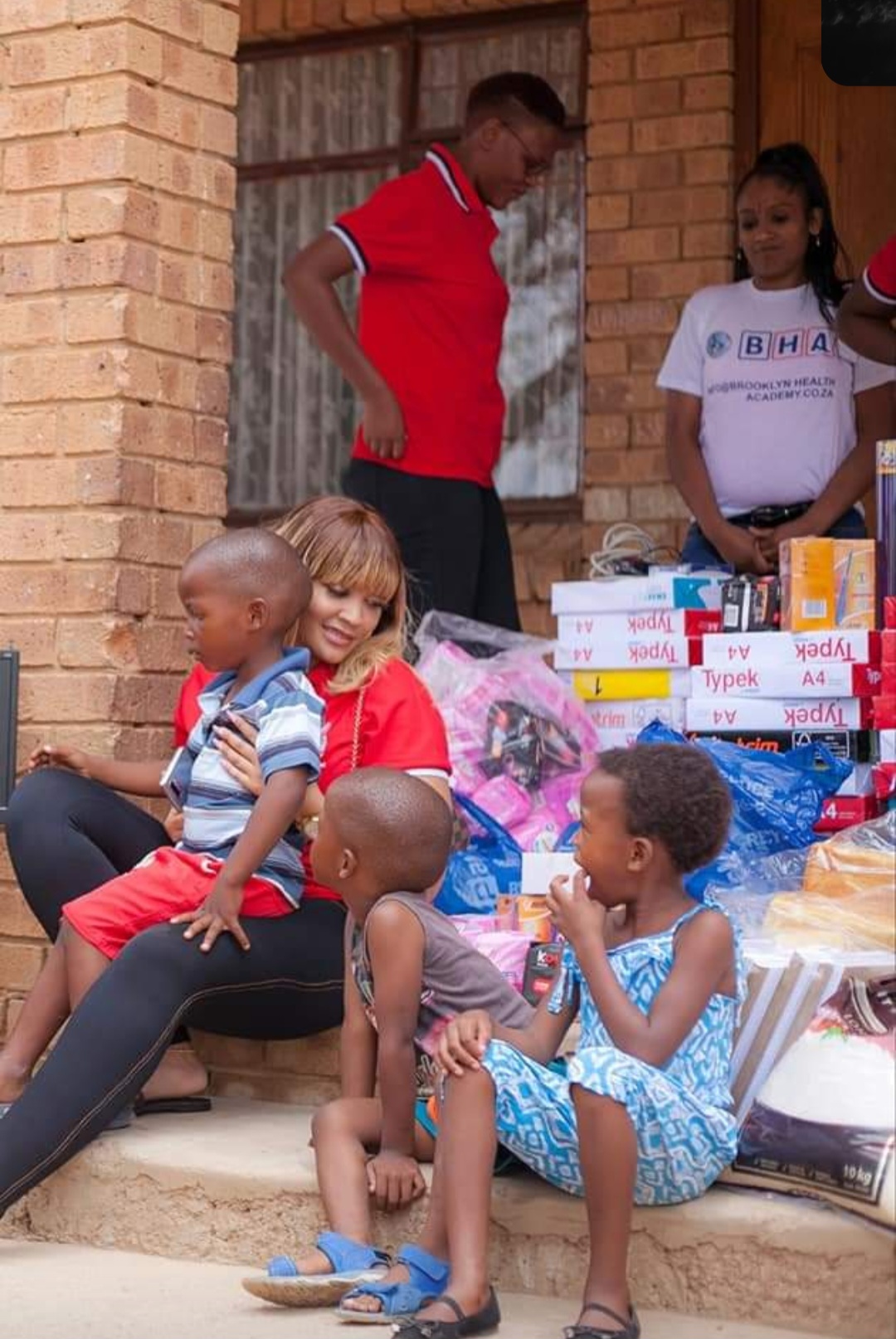 Zari Hassan seated with young children beside stacks of Typek A4 paper, stationery and household staples for a family in need