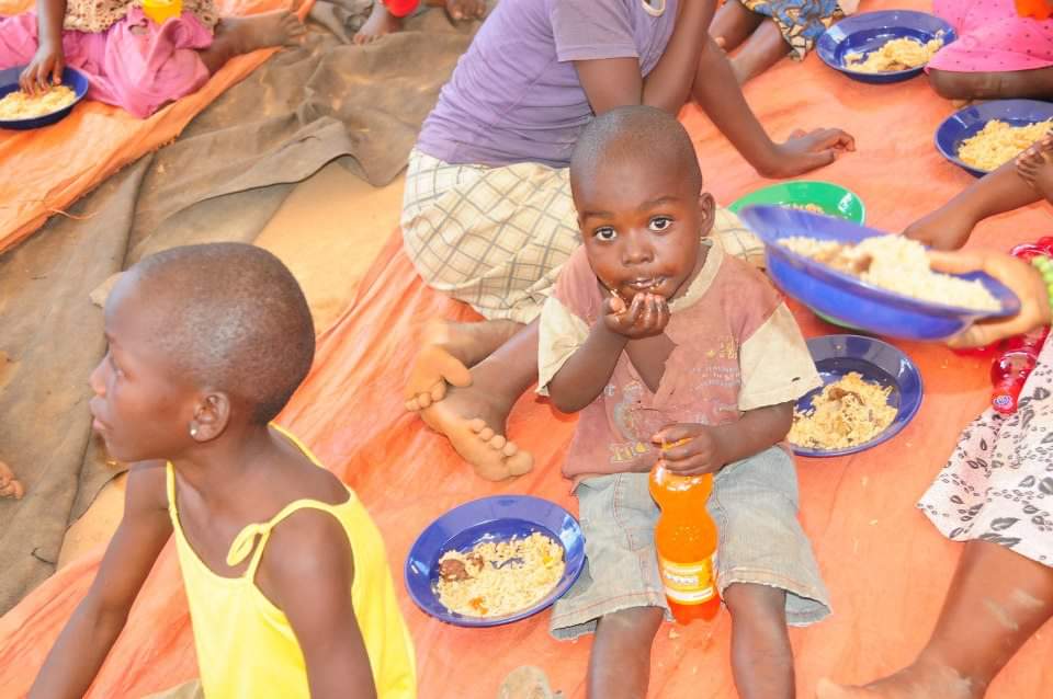 A young child eating a plate of rice and holding a cold drink at a foundation feeding event