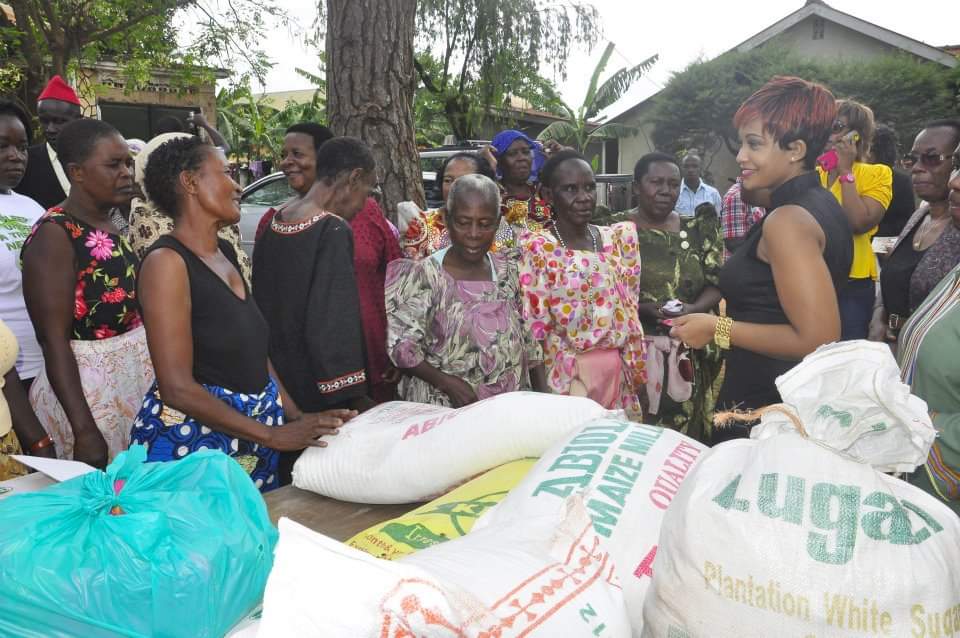Zari Hassan standing with elderly women beside sacks of maize meal and sugar at a community food distribution